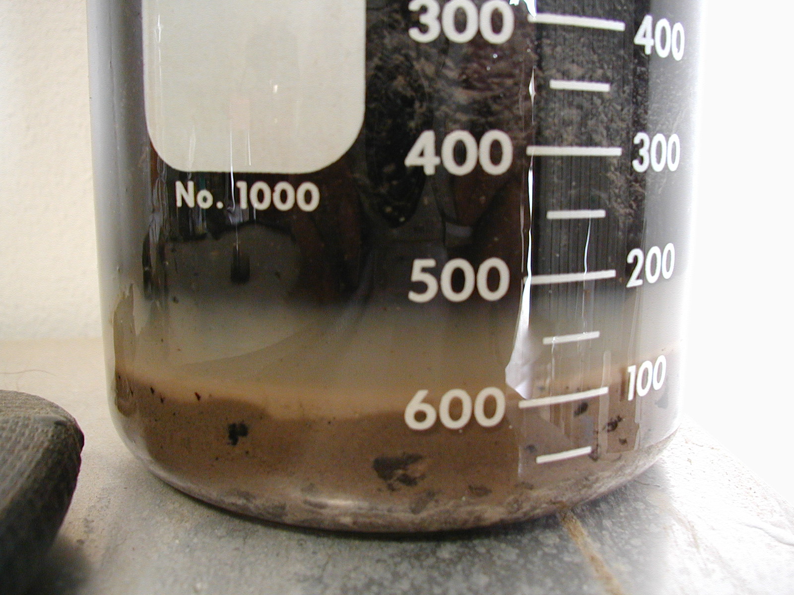 Heavy oil sludge sample in a laboratory beaker during PetroChem treatment evaluation